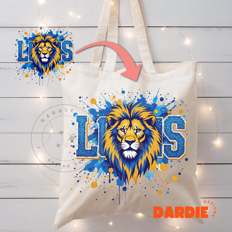 May include: A white canvas tote bag with a blue and yellow lion graphic and the word "LIONS" in blue glitter. The lion is surrounded by blue and yellow paint splatters.