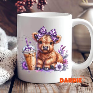 Pu&ograve; includere: Tazza in ceramica bianca con una mucca delle Highlands di colore viola e bianco che indossa un fiocco viola e bianco. La mucca tiene un caff&egrave; freddo viola e bianco. La tazza ha la parola "DARDIE" stampata sul fondo.