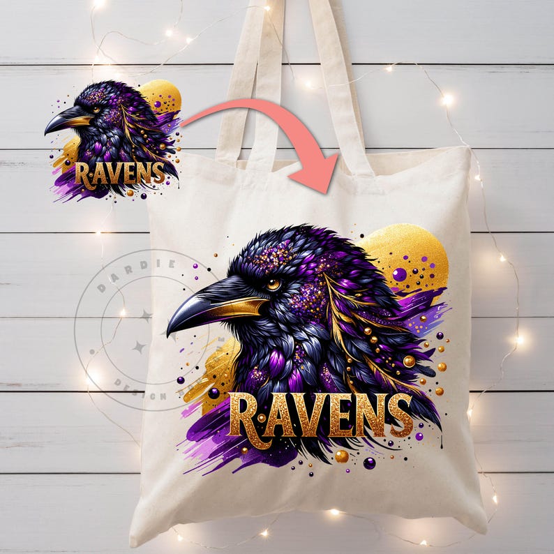 May include: A cream-colored tote bag featuring a detailed illustration of a raven's head. The raven is depicted with purple and gold accents, with the word "RAVENS" in gold lettering. The design includes a gold sun-like shape in the background.