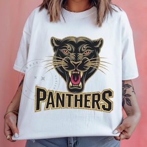 Pode incluir: Camiseta branca com um gr&aacute;fico de pantera negra e letras douradas com glitter que dizem "PANTHERS".