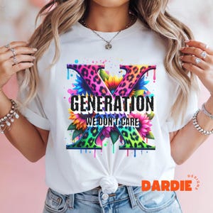 Puede incluir: Camiseta blanca con un gráfico colorido de la letra X hecha de estampado de leopardo y girasoles. El texto "Generation We Don't Care" está impreso debajo de la letra X.