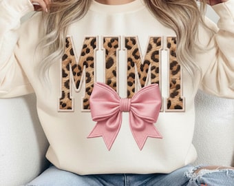May include: Cream-colored sweatshirt with the word "MIMI" in a leopard print design. A pink bow is centered below the text. The sweatshirt is a casual style, suitable for everyday wear.