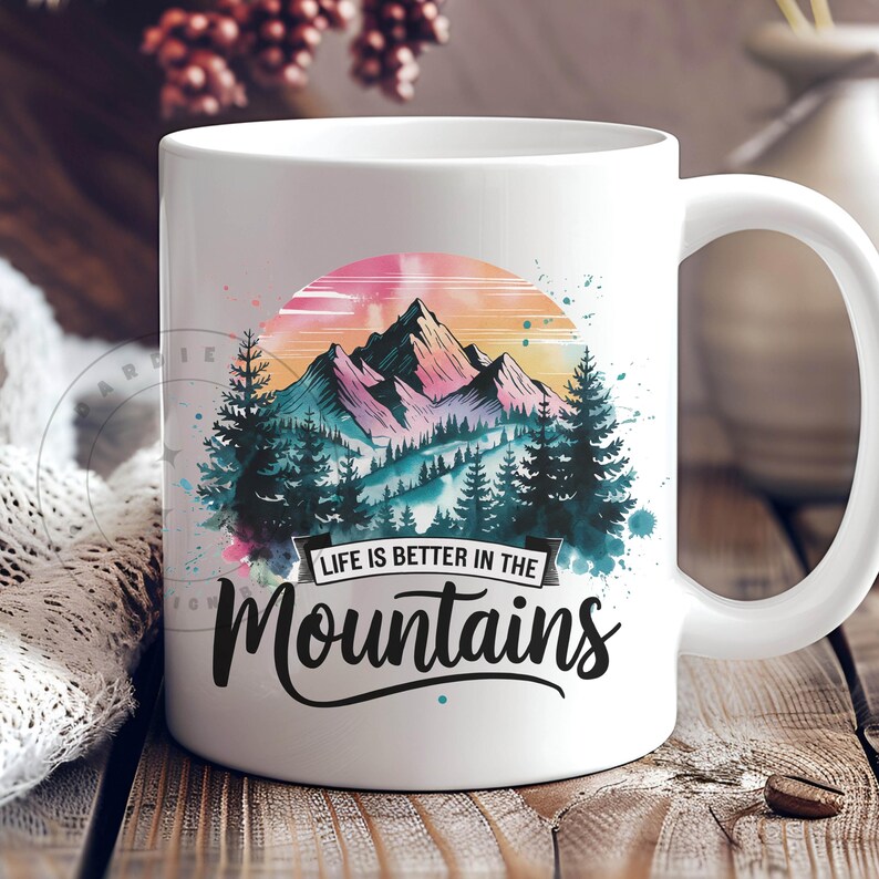 Op de afbeelding: Witte keramische mok met een aquarelontwerp van bergen en bomen. De tekst "Life is better in the mountains" is op de mok gedrukt.