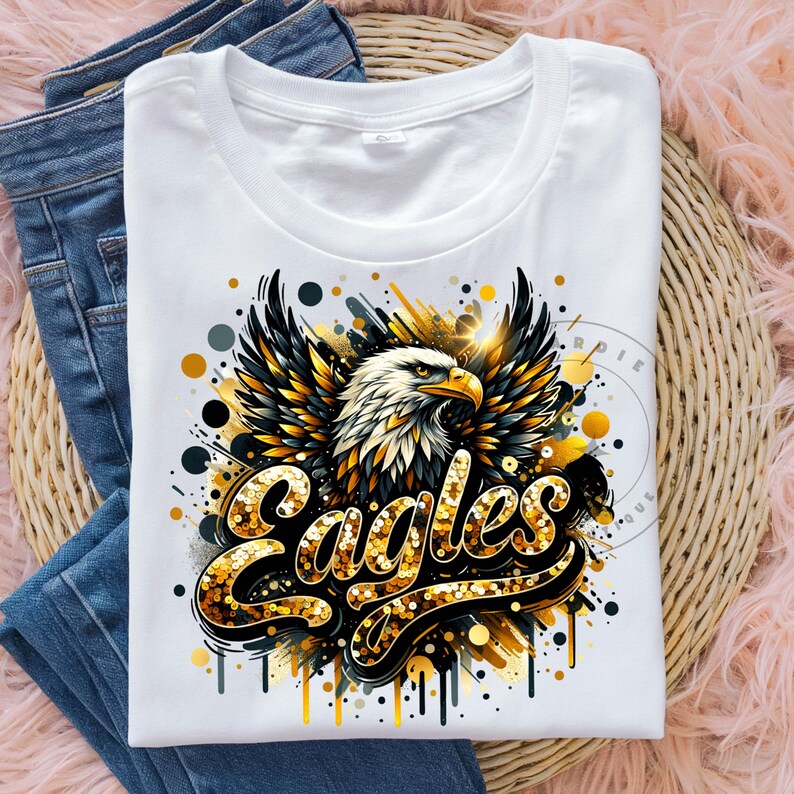 Peut inclure: T-shirt blanc avec un graphique or et noir d'un aigle avec les ailes d&eacute;ploy&eacute;es et le mot "Eagles" en lettres dor&eacute;es paillet&eacute;es.