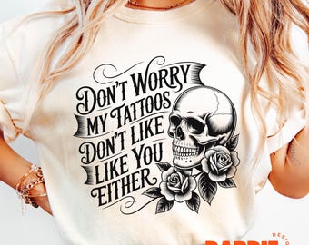 May include: Cream-colored t-shirt featuring a black skull graphic with roses and the text "Don't Worry My Tattoos Don't Like You Either." The design is a bold statement piece.