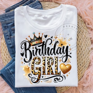 May include: White t-shirt with a gold crown, black lettering that says "Birthday Girl" with a leopard print design, and a gold heart.