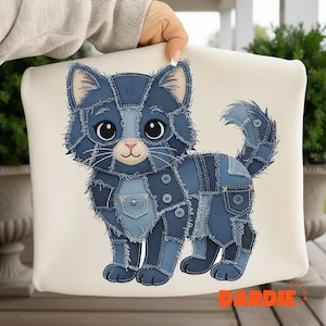 Op de afbeelding: Een decoratief kussen met een blauw denim kattenontwerp. De kat is gemaakt van verschillende denim patches, met knoop- en zakdetails. De kat heeft grote ogen, een roze neus en snorharen. Het kussen staat op een crèmekleurige achtergrond.