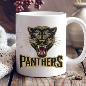 Pode incluir: Caneca de caf&eacute; de cer&acirc;mica branca com um gr&aacute;fico de pantera negra e texto de glitter dourado que diz "PANTHERS".