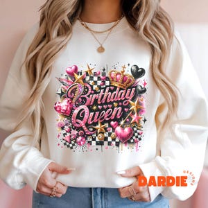 May include: White sweatshirt with a pink and black graphic design featuring a crown, hearts, stars, and the text "Birthday Queen".