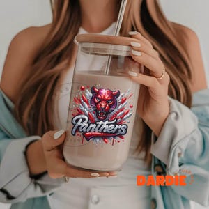 May include: A clear glass tumbler with a red and silver glitter design featuring a panther head and the word "Panthers".