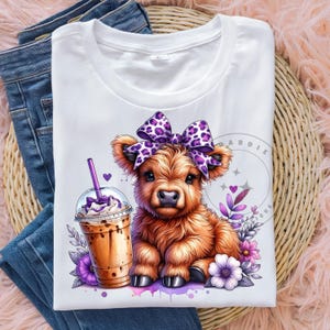 Pu&ograve; includere: Una maglietta bianca con un simpatico cartone animato di mucca Highland che indossa un fiocco viola e bianco a pois. La mucca tiene un drink al caff&egrave; freddo marrone e bianco. Lo sfondo &egrave; un design ad acquerello con fiori viola.