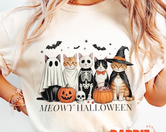 Könnte beinhalten: Cremefarbenes T-Shirt mit einem Halloween-Katzen-Motiv. Das Design zeigt fünf Katzen in Kostümen, darunter ein Geist, ein Skelett und eine Hexe. Der Text "MEOWY HALLOWEEN" ist darunter gedruckt, mit Fledermäusen und Sternen darüber.