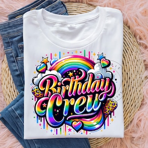 以下が含まれることがあります： 虹、星、ハートのデザインが施された白いTシャツ。"Birthday Crew"というテキストは、カラフルでスタイリッシュなフォントで書かれています。
