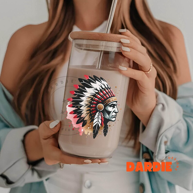 May include: A clear glass tumbler with a brown liquid inside. The tumbler has a brown lid and a straw. A colorful graphic of a Native American chief wearing a headdress is printed on the side of the tumbler.