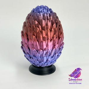 Op de afbeelding: Een 3D-geprint drakenei met een verloop van rode en paarse schubben. Het ei staat op een zwarte voet.
