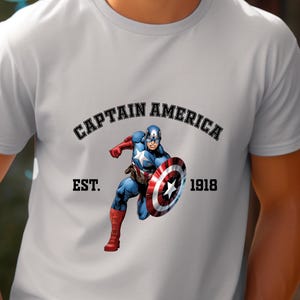 Pu&ograve; includere: T-shirt grigio chiaro con grafica di Captain America con il suo scudo. Il testo "CAPTAIN AMERICA" &egrave; sopra l'immagine, con "EST. 1918" sotto. Il supereroe &egrave; raffigurato in una posa dinamica.