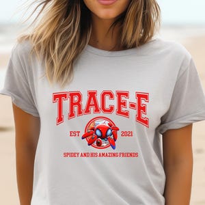 May include: A light gray t-shirt with the text "TRACE-E" in red, along with a cartoon image of Spider-Man. The shirt also features the text "EST 2021" and "SPIDEY AND HIS AMAZING FRIENDS".