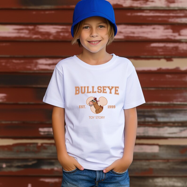 May include: White t-shirt featuring the word "BULLSEYE" in orange lettering, with an image of a cartoon horse and the text "EST. 1999 TOY STORY." The shirt is worn by a person wearing a blue cap.