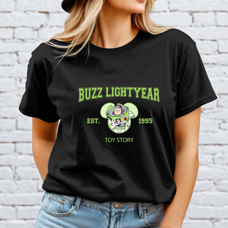 May include: Black t-shirt featuring the text "BUZZ LIGHTYEAR" in green, with a graphic of the character and the words "EST. 1995 TOY STORY". The shirt is a classic crew neck style.