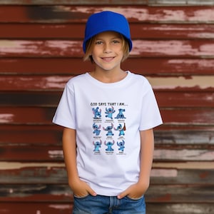 May include: A white t-shirt featuring a graphic of the character Stitch from Lilo & Stitch. The shirt has the text "GOD SAYS THAT I AM..." above a grid of Stitch images with positive affirmations. The child is wearing a blue baseball cap.