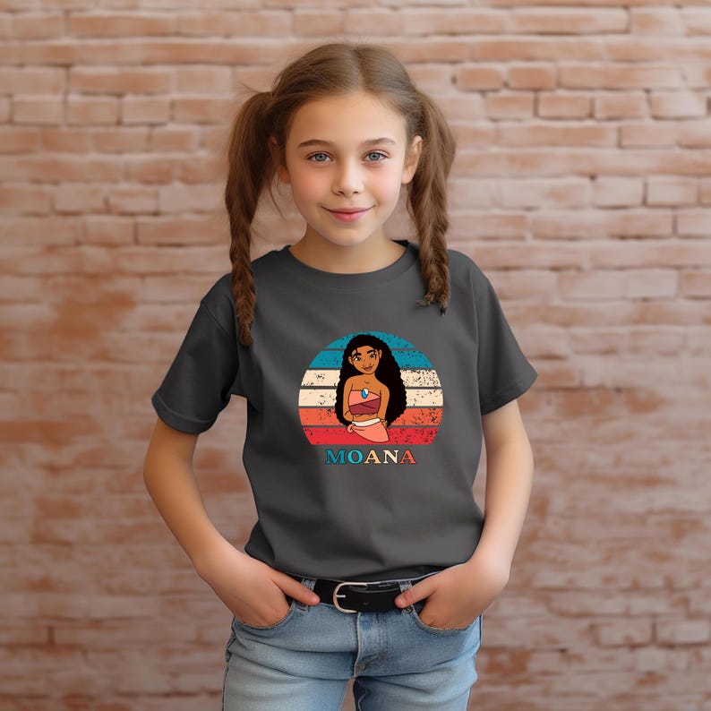 Puede incluir: Una camiseta gris oscuro con un gr&aacute;fico de estilo vintage de Moana, una princesa polinesia, con un fondo de puesta de sol. El texto "MOANA" est&aacute; impreso debajo del gr&aacute;fico.