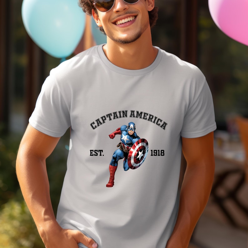 Pu&ograve; includere: T-shirt grigio chiaro con grafica di Captain America con il suo scudo. Il testo "CAPTAIN AMERICA" &egrave; sopra l'immagine, con "EST. 1918" sotto. Il supereroe &egrave; raffigurato in una posa dinamica.