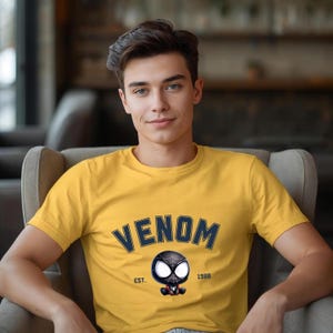 May include: Yellow t-shirt with the word "VENOM" in navy blue arched text. Below the text is a cartoon image of Venom's head, with the text "EST. 1988" below the image. The t-shirt is short-sleeved.