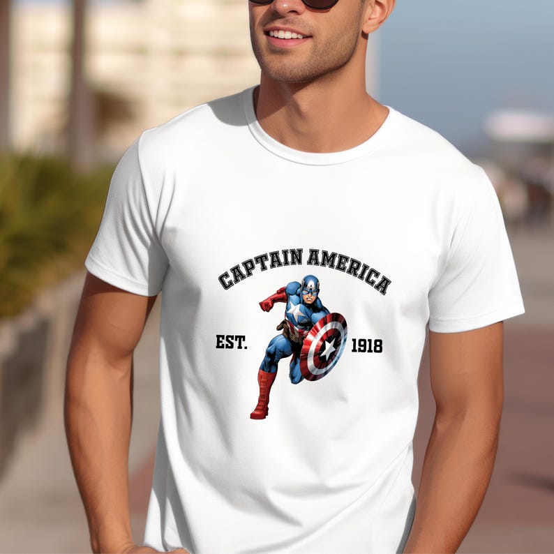 May include: White t-shirt featuring a graphic of Captain America in action, holding his shield. The text "CAPTAIN AMERICA" arches above the image, with "EST. 1918" below. The shirt is a classic crew neck style.