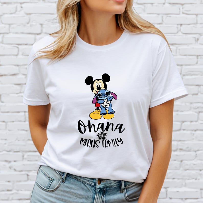 May include: White t-shirt featuring Mickey Mouse and Stitch hugging. Below the characters, the text reads "Ohana Means Family" in black script. The design includes a small flower graphic.
