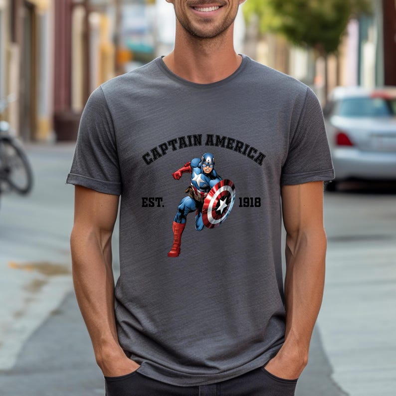 Pu&ograve; includere: T-shirt grigio scuro con grafica di Captain America. La grafica include la scritta "CAPTAIN AMERICA" sopra l'immagine di Captain America con il suo scudo e la scritta "EST. 1918" sotto. La maglietta ha maniche corte.