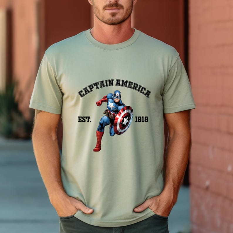 Pu&ograve; includere: T-shirt verde chiaro con grafica di Captain America con il suo scudo. Il testo "CAPTAIN AMERICA" &egrave; sopra l'immagine, con "EST. 1918" sotto. La maglietta &egrave; a girocollo e maniche corte.