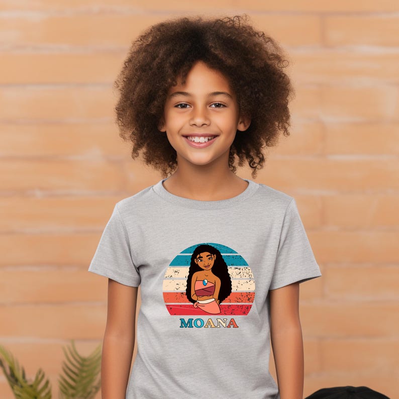 Puede incluir: Una camiseta gris con un gr&aacute;fico de estilo retro de Moana, una princesa de Disney, frente a una puesta de sol. El texto "MOANA" est&aacute; impreso debajo del gr&aacute;fico.