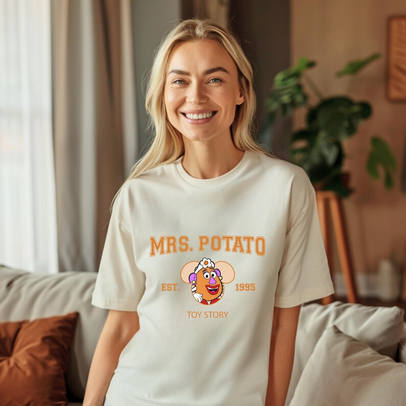 May include: Cream-colored t-shirt featuring the text "MRS. POTATO" in orange, with an illustration of Mrs. Potato Head from Toy Story. The graphic includes the text "EST. 1995" and "TOY STORY" below the character.