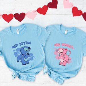 May include: Two light blue t-shirts with cartoon graphics. One shirt says "Her Stitch" with a blue character and a flower. The other says "His Angel" with a pink character. Red and pink heart garland is in the background.