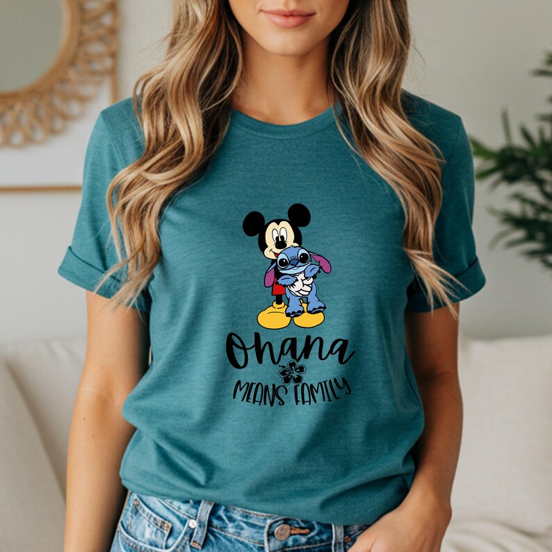 May include: Teal t-shirt featuring Mickey Mouse hugging Stitch, with the words "Ohana Means Family" in black script. The design includes a flower graphic. The shirt has short sleeves and a crew neck.