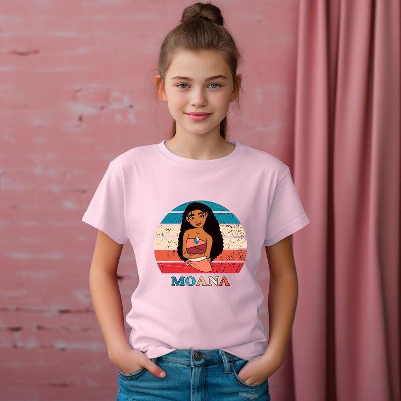 Puede incluir: Una camiseta rosa con un gr&aacute;fico de estilo retro de Moana, una princesa polinesia de la pel&iacute;cula de Disney Moana. El gr&aacute;fico presenta a Moana de pie frente a una puesta de sol con el texto "Moana" debajo.