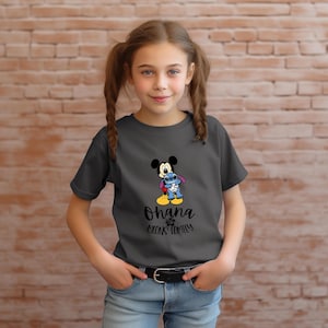 May include: A charcoal gray t-shirt featuring a graphic of Mickey Mouse and Stitch hugging. The text "Ohana means family" is printed below the characters. The shirt is worn by a young person.
