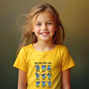 May include: A yellow t-shirt featuring a graphic of the character Stitch from Lilo & Stitch. The shirt has the text "GOD SAYS THAT I AM..." above a series of Stitch illustrations with positive affirmations. The girl is smiling.