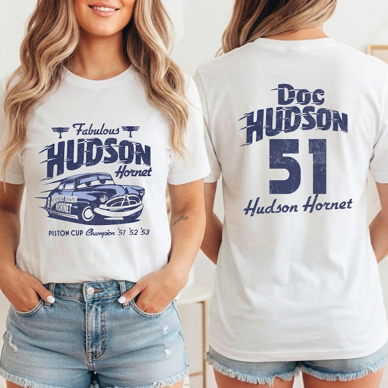 May include: White t-shirt featuring a blue graphic of a Hudson Hornet car with the text "Fabulous Hudson Hornet" and "Piston Cup Champion '51 '52 '53". The back of the shirt displays "Doc Hudson 51 Hudson Hornet".