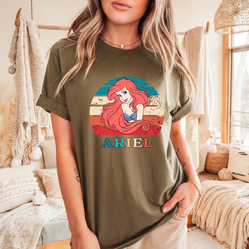 Puede incluir: Una camiseta verde con un gr&aacute;fico de estilo vintage de Ariel, la Sirenita, con el texto "ARIEL" debajo del gr&aacute;fico.