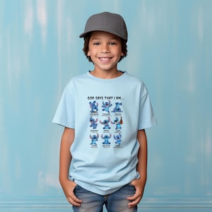 May include: A light blue t-shirt featuring the character Stitch from Lilo & Stitch. The shirt has the text "GOD SAYS THAT I AM..." above a grid of Stitch images with positive affirmations like "Empowered" and "Loved".