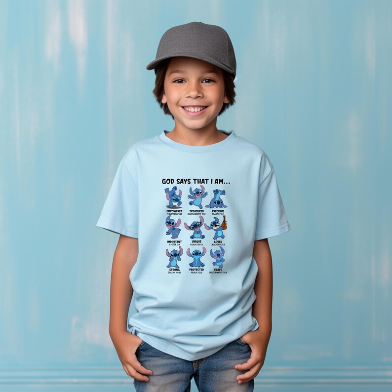 May include: A light blue t-shirt featuring the character Stitch from Lilo & Stitch. The shirt has the text "GOD SAYS THAT I AM..." above a grid of Stitch images with positive affirmations like "Empowered" and "Loved".