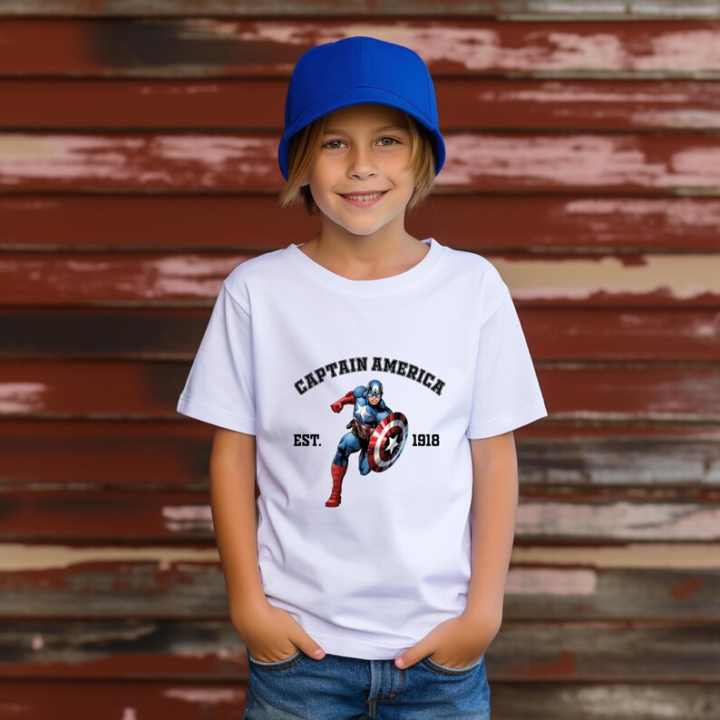 Pu&ograve; includere: Una maglietta bianca con il logo di Captain America e la scritta "CAPTAIN AMERICA EST. 1918". La maglietta presenta una grafica di Captain America con il suo scudo. La persona nell'immagine indossa un berretto da baseball blu e jeans blu.