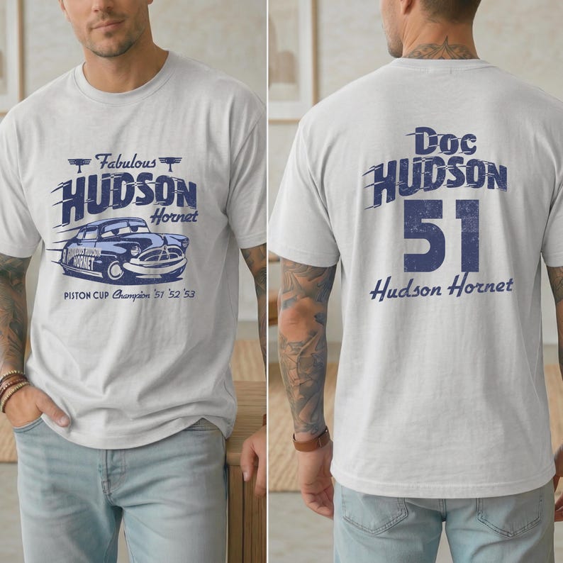 May include: Light gray t-shirt featuring a blue graphic of a vintage Hudson Hornet car with the text "Fabulous Hudson Hornet" and "Piston Cup Champion '51 '52 '53" on the front. The back of the shirt displays "Doc Hudson 51 Hudson Hornet".
