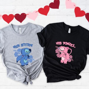 May include: Two t-shirts, one grey and one black, with cartoon character graphics. The grey shirt says "Her Stitch" and features a blue character. The black shirt says "His Angel" and features a pink character. Red and pink heart garland in the background.