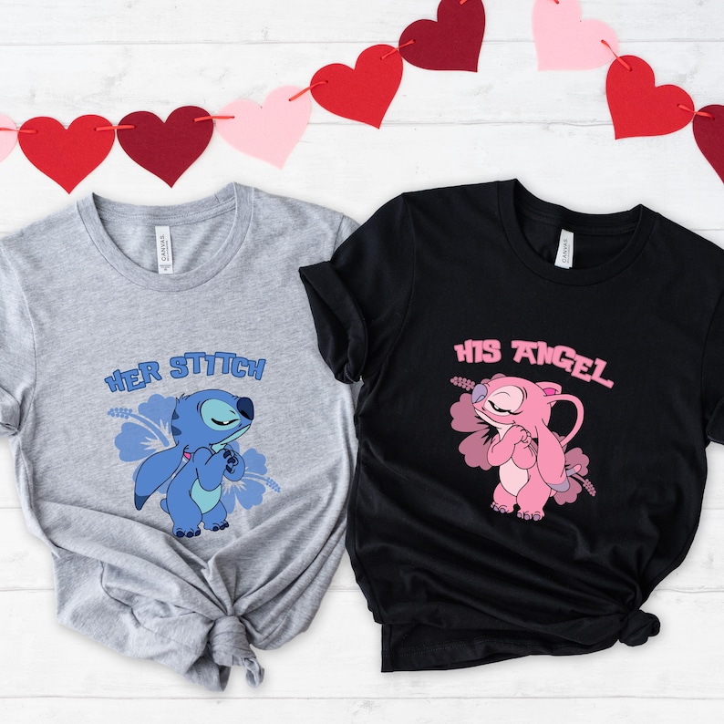 May include: Two t-shirts, one grey and one black, with cartoon character graphics. The grey shirt says "Her Stitch" and features a blue character. The black shirt says "His Angel" and features a pink character. Red and pink heart garland in the background.