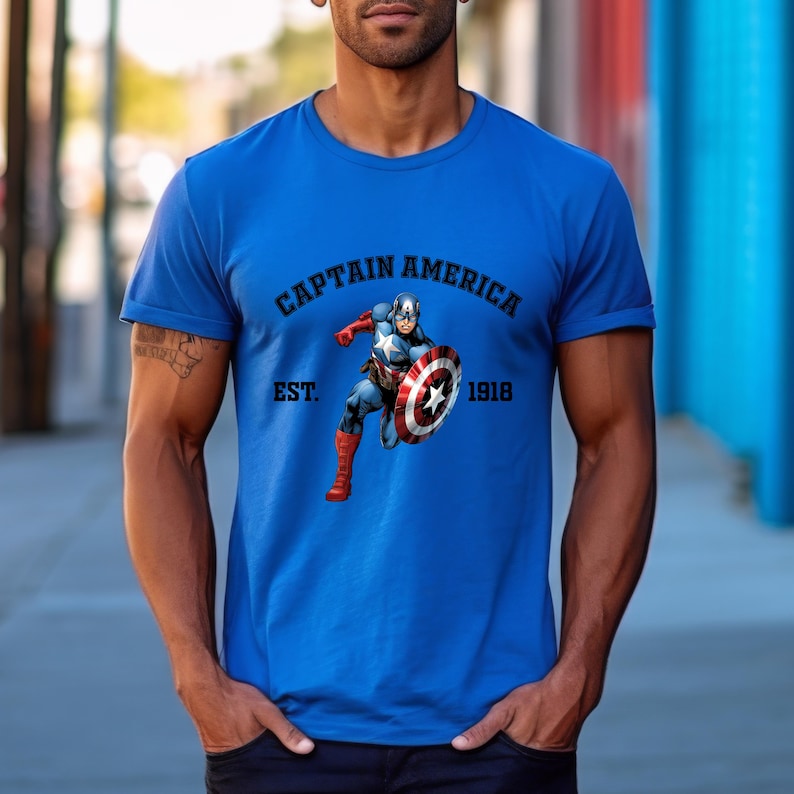Pu&ograve; includere: Una maglietta blu con una grafica di Captain America con il suo scudo. Il testo "CAPTAIN AMERICA" &egrave; sopra l'immagine, con "EST. 1918" sotto. La maglietta &egrave; di colore blu unito.