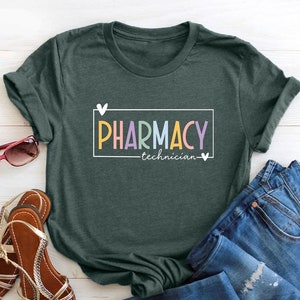 May include: A dark green t-shirt with a white box and the text "PHARMACY technician" in colorful letters. The text is surrounded by two white hearts.