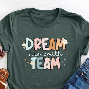 Pode incluir: Uma camiseta verde com o texto "DREAM mrs. smith TEAM" em letras coloridas com flores e glitter.