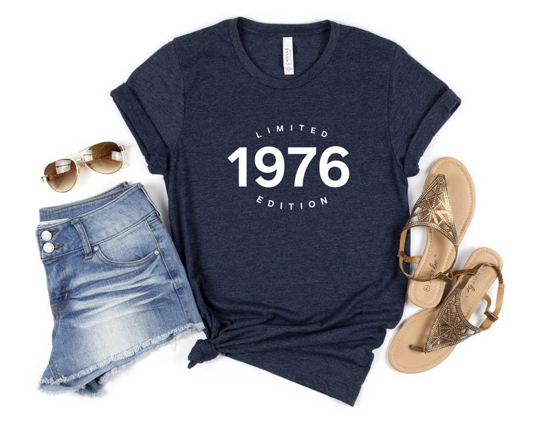 K&ouml;nnte beinhalten: Marineblaues T-Shirt mit wei&szlig;em Aufdruck "LIMITED 1976 EDITION". Dazu Jeansshorts, Sonnenbrille und goldene Sandalen. Ein l&auml;ssiges Outfit, passend f&uuml;r einen Geburtstag oder ein Jubil&auml;um.